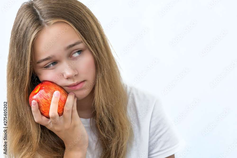 Portrait of upset dreaming young beautiful girl in white shirt , holding red apple in the hands near the cheek unhappy face on white background. Isolated ,copy space Portrait of upset dreaming young beautiful girl in white shirt , holding red apple in the hands near the cheek unhappy face on white background. Isolated ,copy space