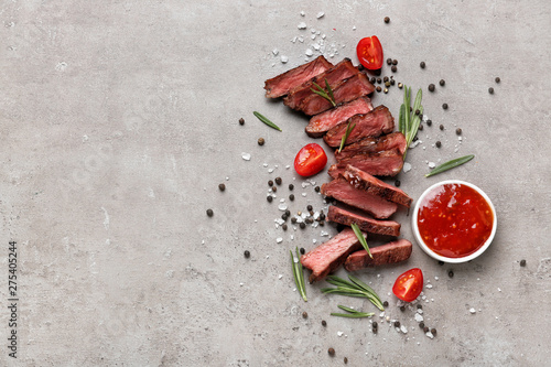 Fototapeta Naklejka Na Ścianę i Meble -  Slices of tasty grilled meat with sauce and spices on grey background
