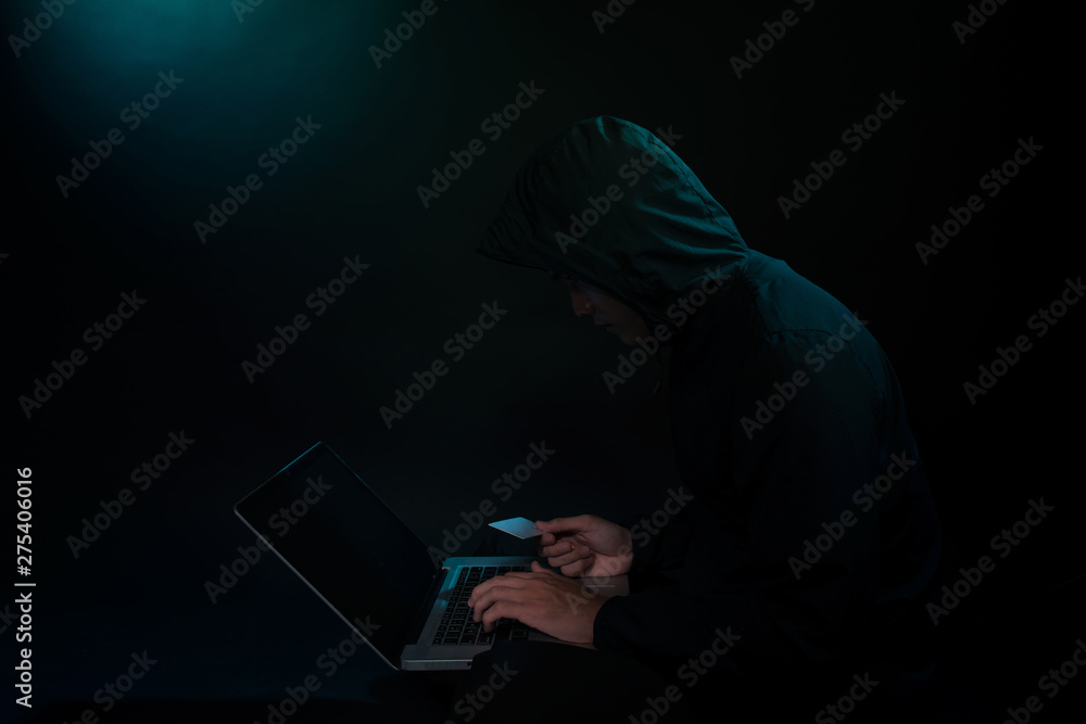 Internet Theft - a man holding a credit card while sat behind a laptop Internet Theft - a man holding a credit card while sat behind a laptop