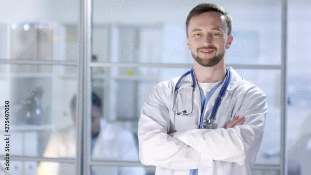 Waist-up portrait shot of middle-aged Caucasian physician, dressed in hospital uniform and lab coat with stethoscope, posing for photos with crossed arms, looking at camera and smiling confidently Waist-up portrait shot of middle-aged Caucasian physician, dressed in hospital uniform and lab coat with stethoscope, posing for photos with crossed arms, looking at camera and smiling confidently