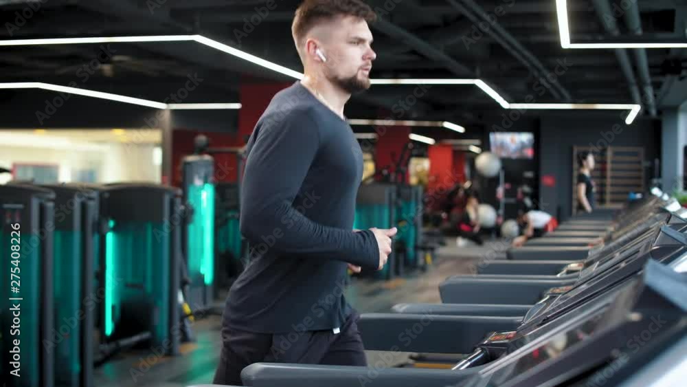 Gym, man athlete in wireless headphones running on a treadmill, aerobic exercise and endurance training, slow motion. Gym, man athlete in wireless headphones running on a treadmill, aerobic exercise and endurance training, slow motion.