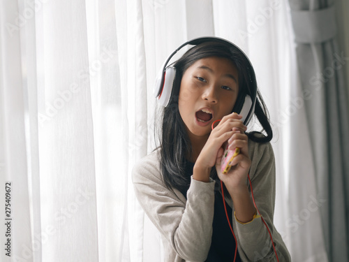 Happy Asian girl using smartphone and singing a song near window at home.