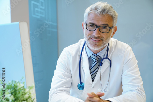 Portrait of handsome mature doctor sitting at desk in modern office