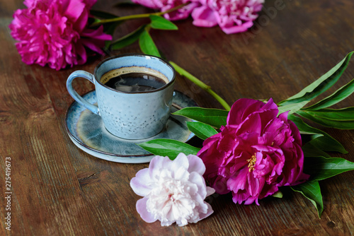 A Cup of coffee and peonies on a dark wooden table. Summer morning, romantic mood.