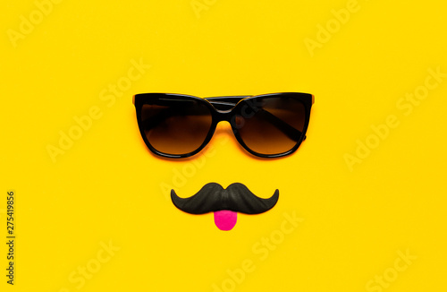 Creative party decoration concept. Black mustache, Sunglasses, props for photo booths, carnival parties on yellow background top view flat lay copy space. Father's day, Men's health awareness month
