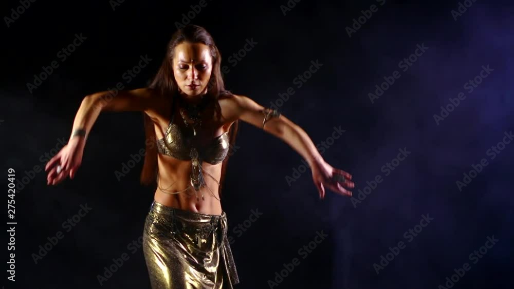 Portrait sexy close-up girl who dances an Oriental belly dance on a black smoky background, she is wearing an Oriental costume, she is illuminated by light. Portrait sexy close-up girl who dances an Oriental belly dance on a black smoky background, she is wearing an Oriental costume, she is illuminated by light.