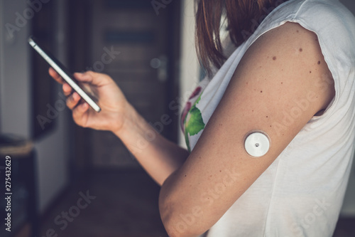 Foto Woman checking glucose level with new technology remote sensor and mobile phone, sensor checkup glucose levels without blood