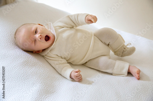 2-month-old baby in white yagging layette lying on his back in a bed. photo