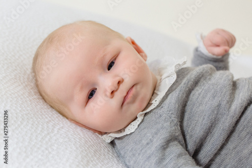 Close-up of a young infant in grey layette of 2 months elongate on a whitebed. photo