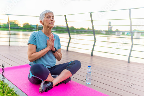 Mature woman practicing yoga in the park. Senior women in yoga position at nature. Spring season. Mature woman in yoga position meditates near river at sunset