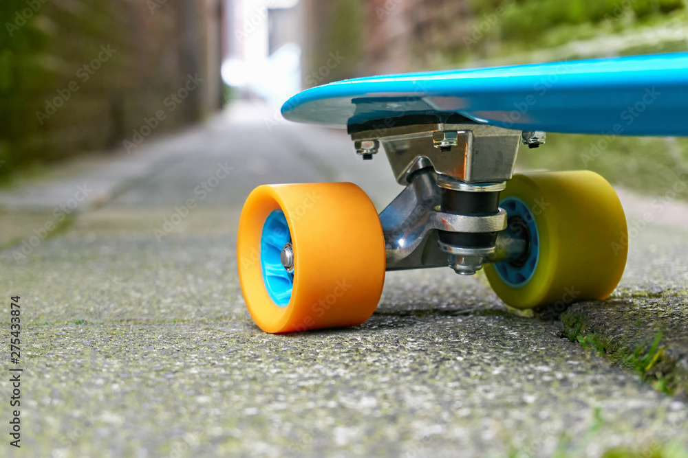 Front of blue plastic mini cruiser penny board or skateboard with yellow  and orange wheels on concrete tiles in an alley with light at the end. Low  perspective, no people. Photos