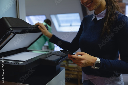 Businesswoman using mobile phone while holding xerox copy machine in hand