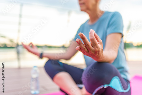 Fitness sport woman in fashion sportswear doing yoga fitness exercise outdoor. Mature woman in yoga position meditates near river at sunset. Mature woman doing yoga at park