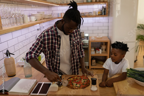  Son watching his father while cutting pizza with pizza cutter in kitchen photo