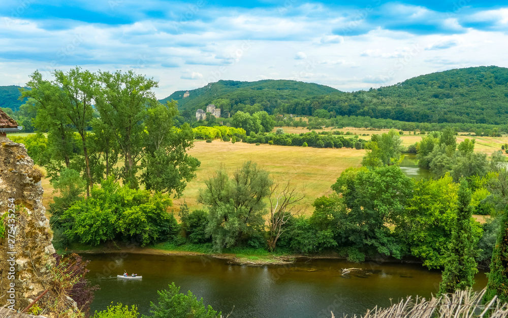 Beynac-et-Cazenac, Dordogne/ France: typical landscape at Perigord with a canoe by the river Dordogne and the Castle of Castelnaud-la-Chapelle in the distance