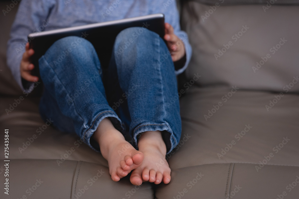 Small boy using digital tablet while sitting on sofa at home Small boy using digital tablet while sitting on sofa at home