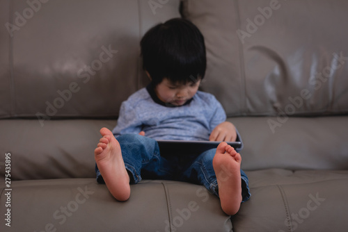 Small boy using digital tablet while sitting on sofa at home photo