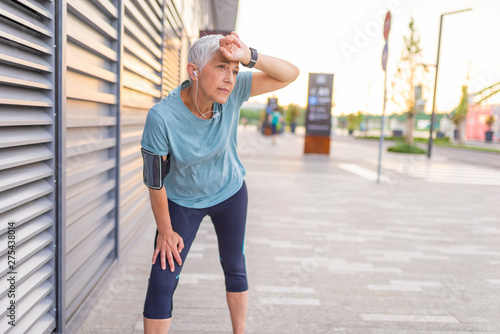  Proud mature woman stretching in the park. Senior active woman completing her daily routine workout. Tired mature sportswoman leaning on bent knees