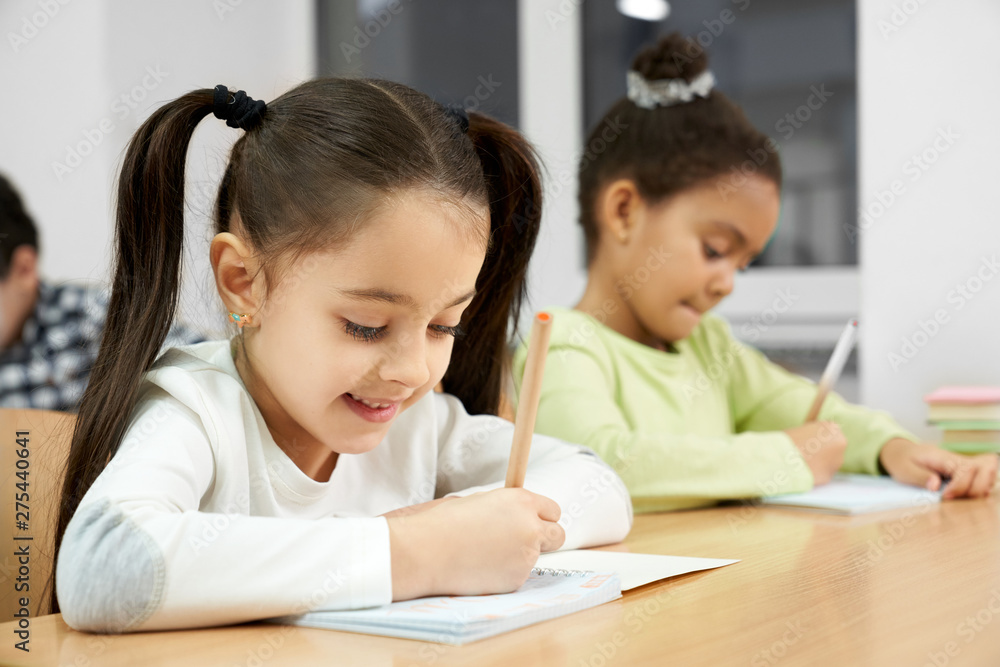 Pretty girls sitting at desk in class, writing in copybook. Pretty girls sitting at desk in class, writing in copybook.