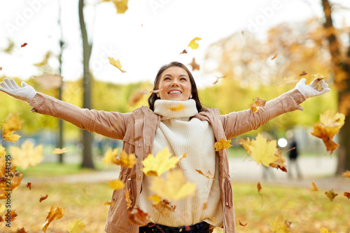 season and people concept - happy young woman throwing maple leaves and having fun in autumn park