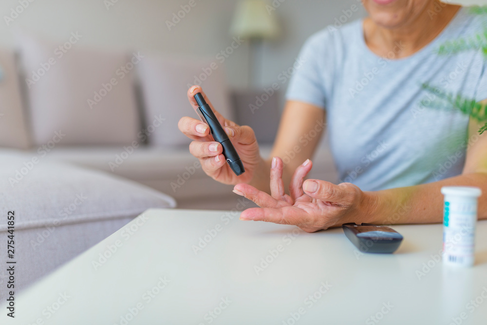 Fototapeta premium Close up of woman hands using lancet on finger to check blood sugar level by Glucose meter, Healthcare Medical and Check up, Medicine, diabetes, glycemia, health care and people concept