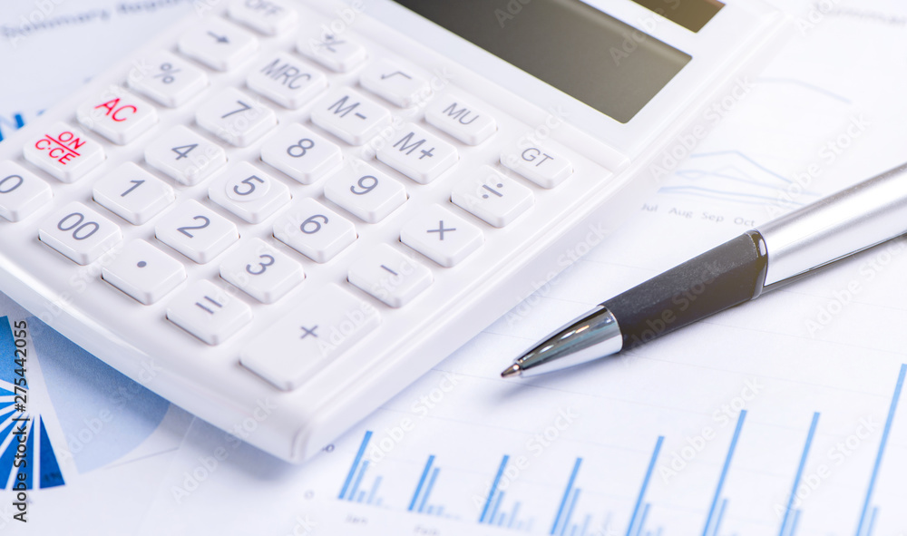 White calculator and report with chart and graph, concept of annual financial profit overview, banking and investment, copy space, macro, close up White calculator and report with chart and graph, concept of annual financial profit overview, banking and investment, copy space, macro, close up
