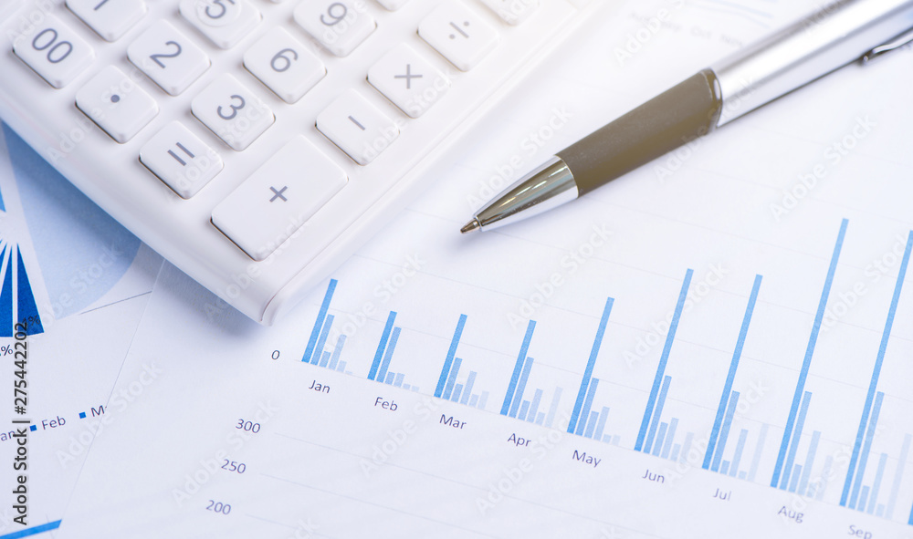 White calculator and report with chart and graph, concept of annual financial profit overview, banking and investment, copy space, macro, close up White calculator and report with chart and graph, concept of annual financial profit overview, banking and investment, copy space, macro, close up