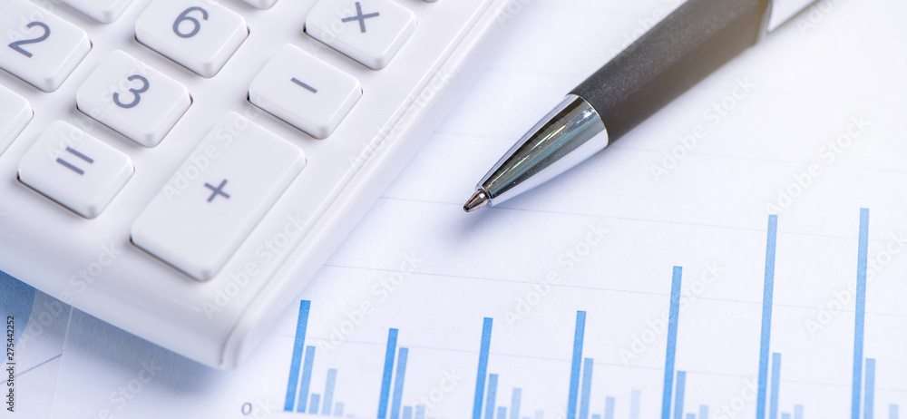 White calculator and report with chart and graph, concept of annual financial profit overview, banking and investment, copy space, macro, close up White calculator and report with chart and graph, concept of annual financial profit overview, banking and investment, copy space, macro, close up