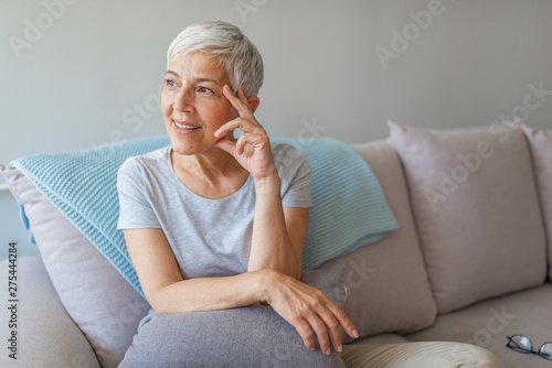Happy senior woman on couch. Portrait of smiling mature woman sitting on sofa. Mature woman smiling. Portrait of beautiful mature woman relaxing by the window.
