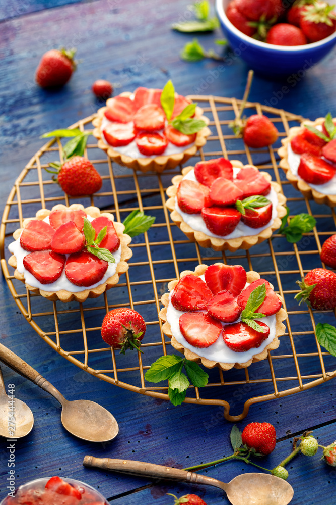 Φωτογραφία Strawberry tarts, small shortcrust tarts with the addition of cream cheese, fresh strawberries and mint on cooling tray on a dark blue table