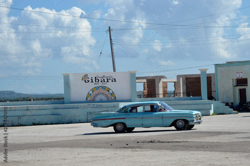 Cuba, Gibara, an old blue 50s American car passes in front of the sign