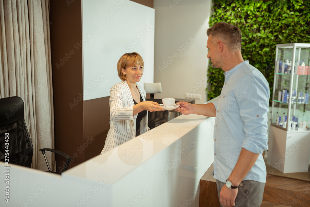Pleasant administrator giving client the cup of tea Pleasant administrator giving client the cup of tea