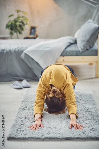 Brunette doing Extended Child's yoga posture on the rug in bedroom.