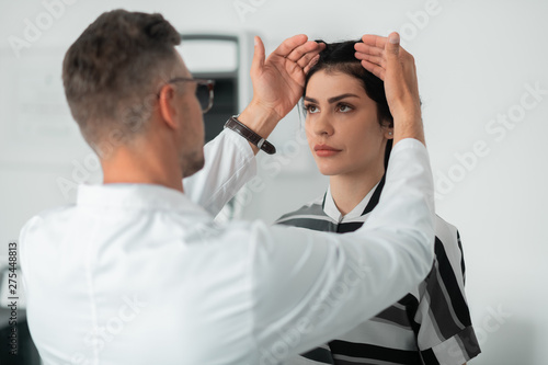 Plastic surgeon wearing glasses examining face of client photo