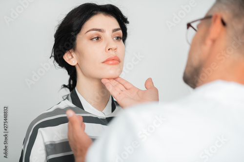 Plastic surgeon wearing glasses touching face of client photo