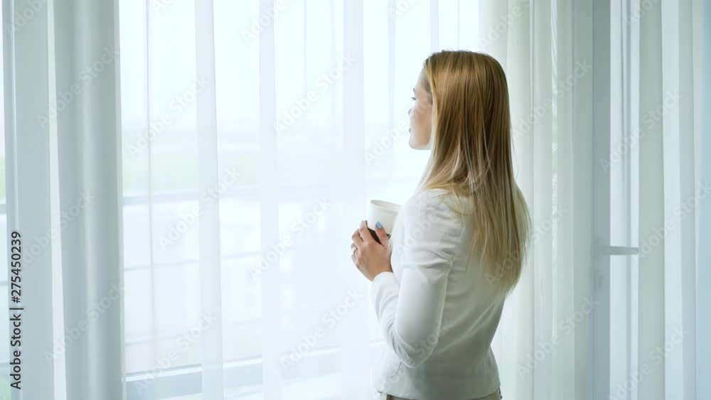 zoom in happy young married woman drinks tea and day dreams in front of window zoom in happy young married woman drinks tea and day dreams in front of window