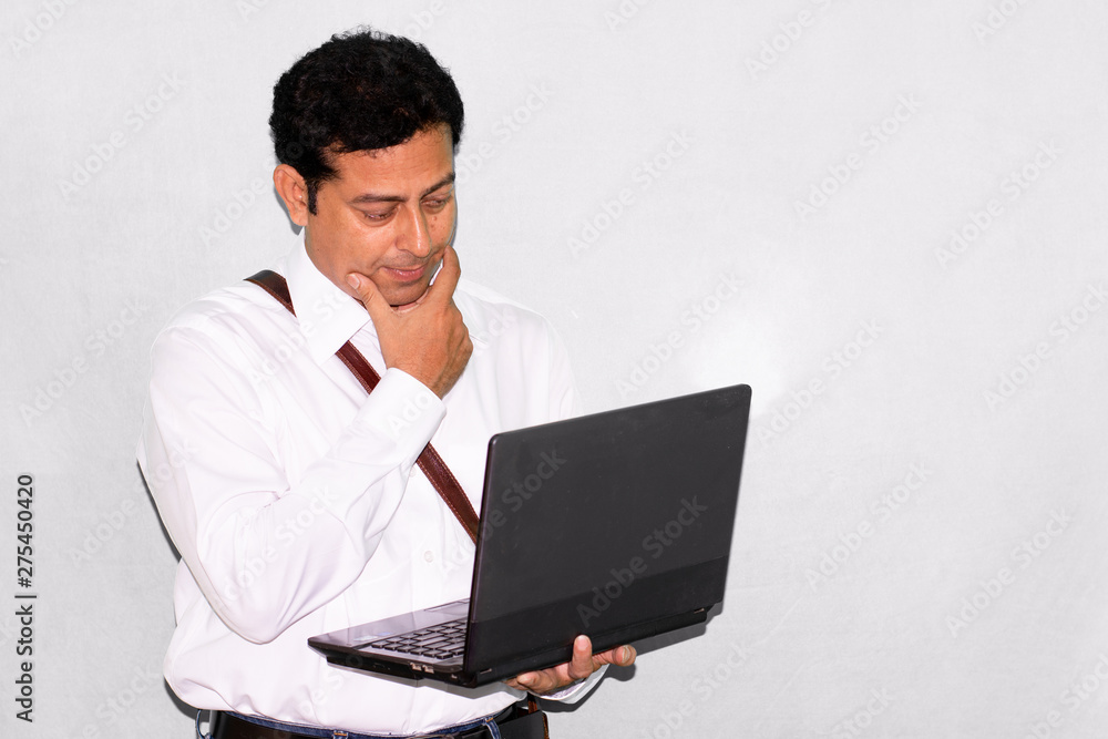 Portrait of Indian businessman man using laptop or computer in studio on white/gray background. Portrait of Indian businessman man using laptop or computer in studio on white/gray background.