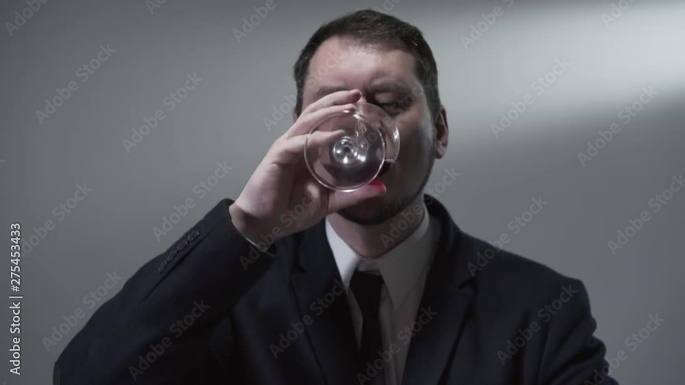 Serious confident gentleman saluting with a glass of red wine and drinking a sip of alcohol looking into the camera. The boss relaxing. Studio shot Serious confident gentleman saluting with a glass of red wine and drinking a sip of alcohol looking into the camera. The boss relaxing. Studio shot