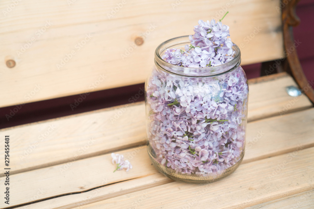 Lilac flowers in a jar on a bench of natural wood for the preparation of alcoholic tincture of lilac to strengthen the immune system and healing the body. Lilac flowers in a jar on a bench of natural wood for the preparation of alcoholic tincture of lilac to strengthen the immune system and healing the body.