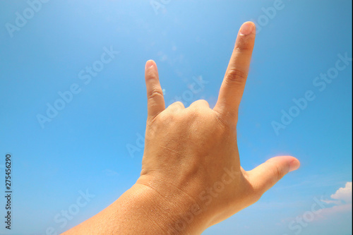 Hand sign of love and showing fingers means I love you on blue sky with sunlight and copty space.