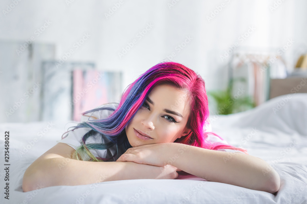 beautiful girl with colorful hair looking at camera and laying in bed - obrazy, fototapety, plakaty 