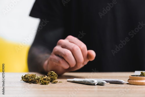 selective focus of weed, joints and herb grinder near man sitting at table