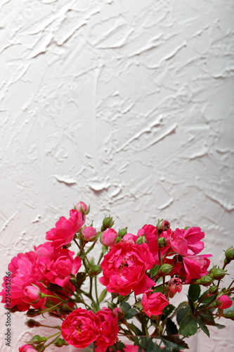 Fototapeta Naklejka Na Ścianę i Meble -  Bouquet of crimson roses in a glass vase with a bow. Against the background of white wall with decorative plaster.