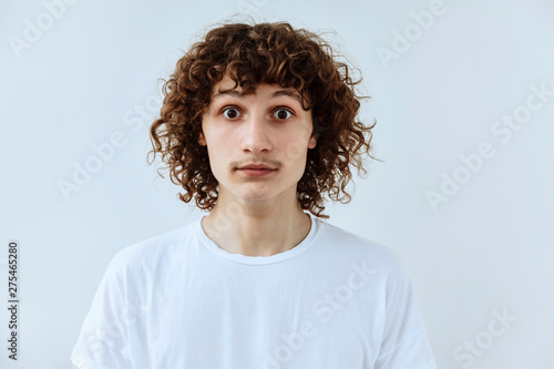 Surprised,shock ,unbelievable emotion. Curly teen guy face portrait agaist white backgraund.