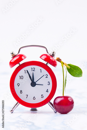 Time for cherry fruits. Red  clock with fresh red cherries on the marble table.