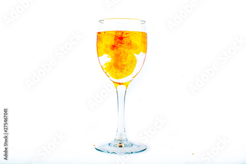 Orange food coloring diffuse in water inside wine glass with empty copyspace area for slogan or advertising text message, over isolated white background.