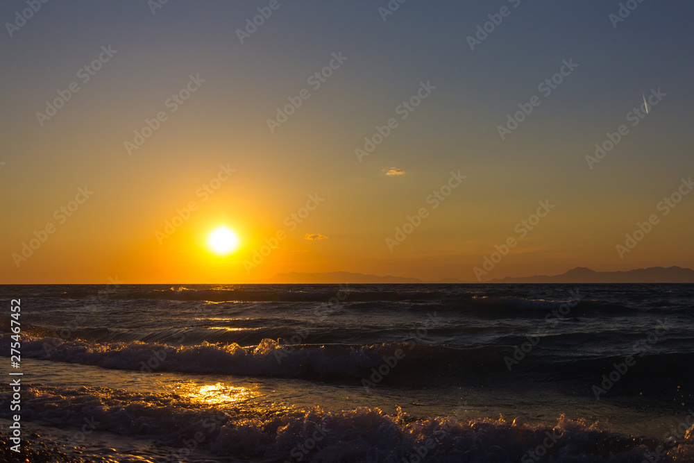 Colorful empty seascape with shiny sea over cloudy sky and sun during sunset in Rhodes, Greece
