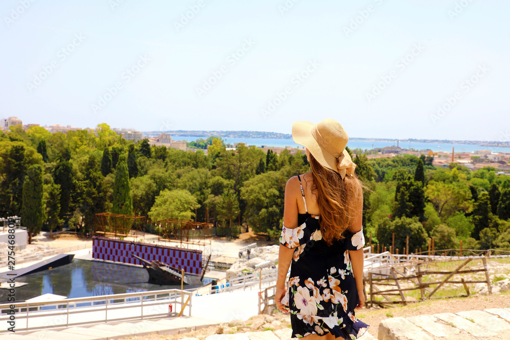 Portrait of young elegant woman with hat and flowered dress in the stands of Syracuse (Siracusa) Greek theatre, Sicily, Italy