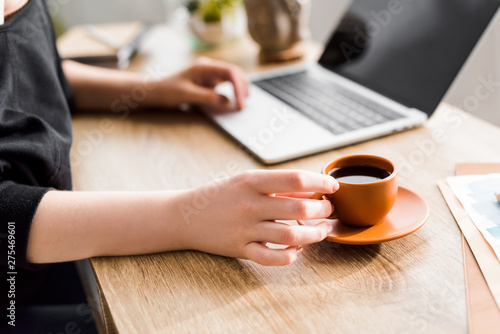 cropped view of woman holding cup of coffee and sitting at table