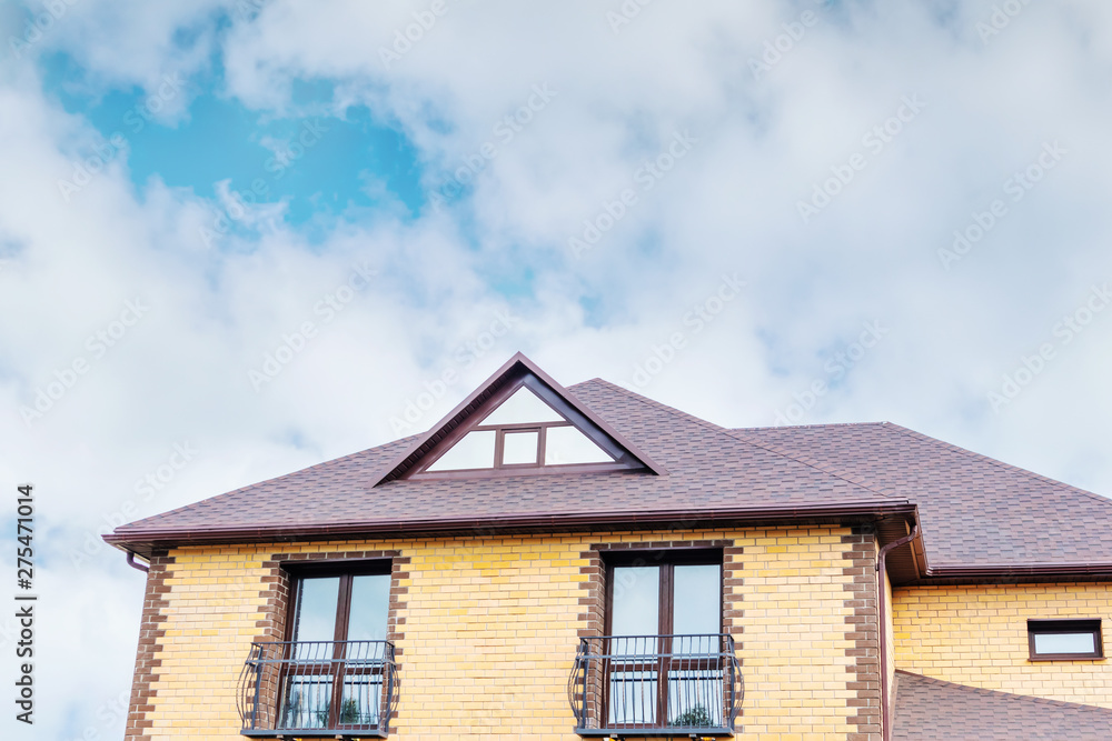 The triangular roof of the house is pastel yellow and brown against a blue sky with light clouds. Bright sunny daylight. Place for text, minimalism. The concept of building houses, cottages.